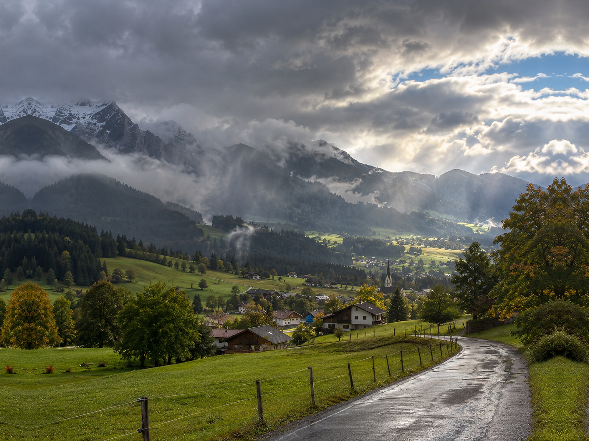 Österreichische Alpenlandschaft mit tiefen Wolken, nasser Straße und herbstlichen Aufhellungen