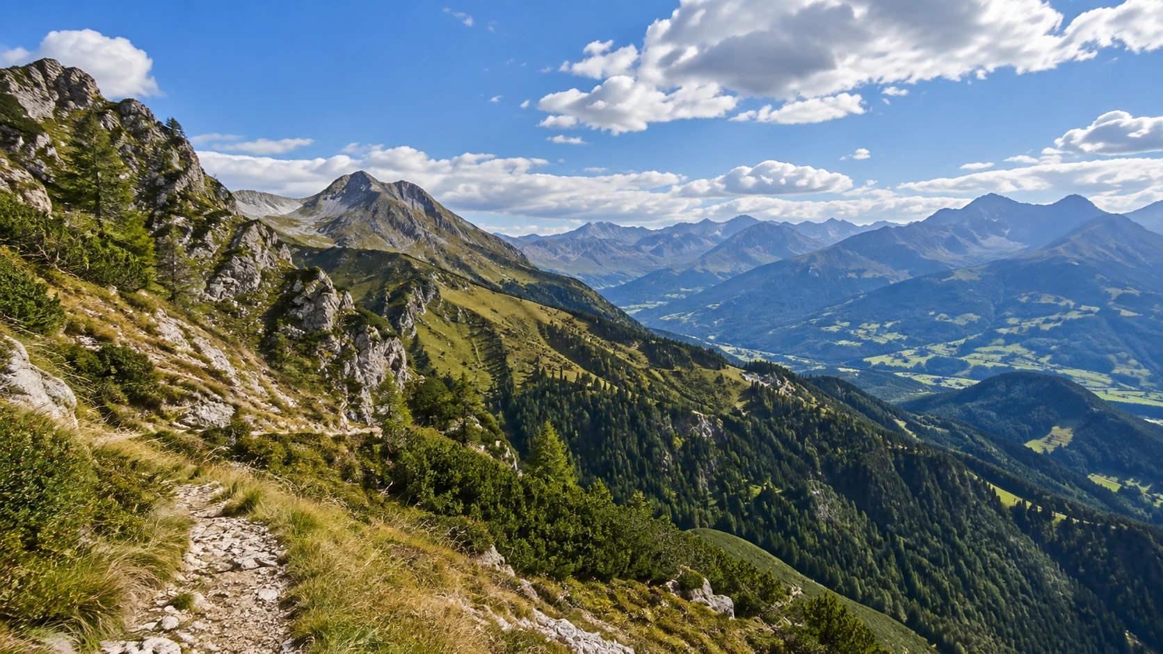 Schneefreier österreichischer Alpenweg über grünen und felsigen Hängen bei guter Sicht.
