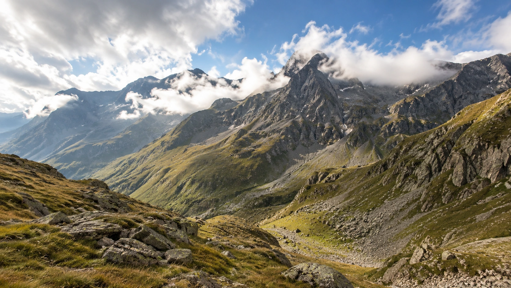 Alpine Gipfel und Höhenzüge unter aufgelockerter, teils dichter Bewölkung.