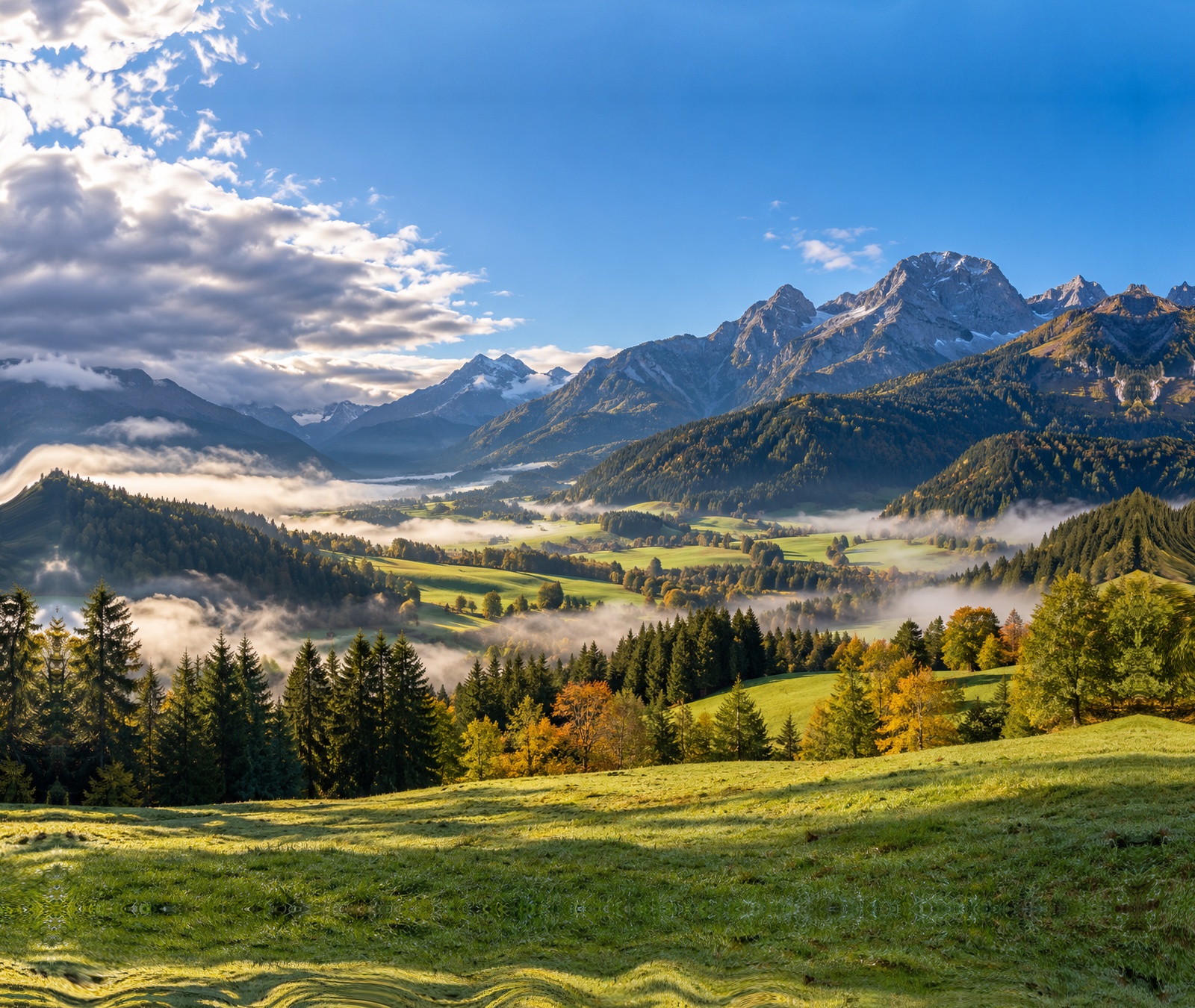 Österreichisches Alpental mit Frühnebel, Sonne und herbstlichen Wiesen