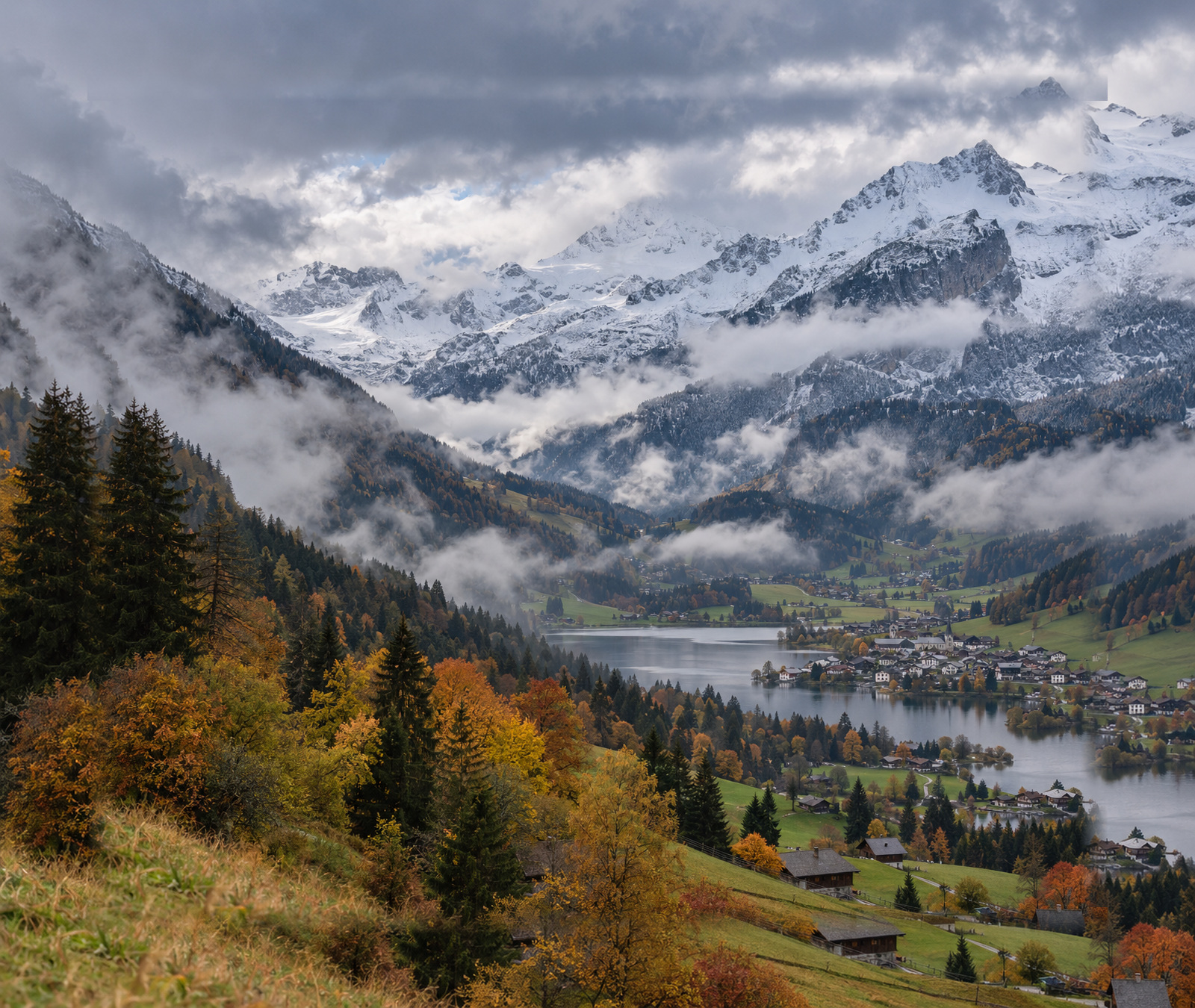 Österreichisches Alpental im Herbst mit dichter werdenden Frontwolken und frischem Schnee auf den hohen Gipfeln.